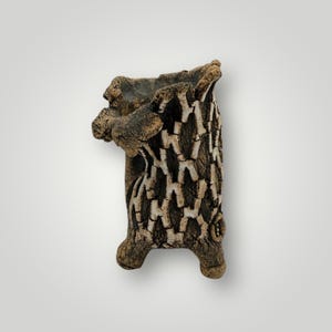 May include: A handcrafted, textured ceramic vase with a unique, organic design. The vase features a dark brown and beige color palette, with a bark-like texture and a three-legged base. The opening is irregular, adding to its rustic charm.