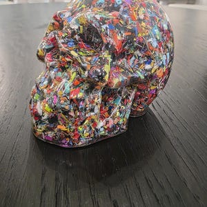 May include: A human skull sculpture made of clear resin embedded with a dense mixture of multicolored plastic fragments, including red, blue, yellow, green, and black pieces, creating a vibrant, confetti-like appearance throughout the entire form.