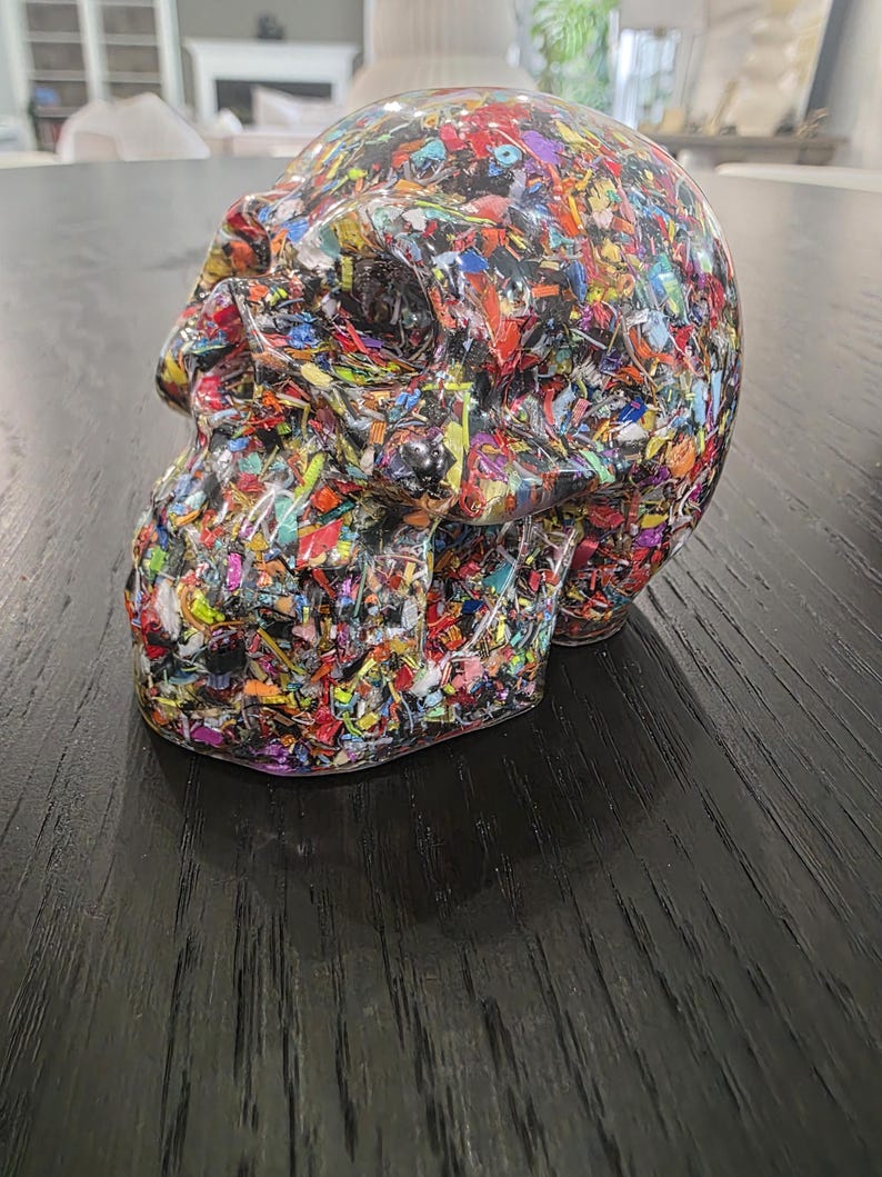 May include: A human skull sculpture made of clear resin embedded with a dense mixture of multicolored plastic fragments, including red, blue, yellow, green, and black pieces, creating a vibrant, confetti-like appearance throughout the entire form.