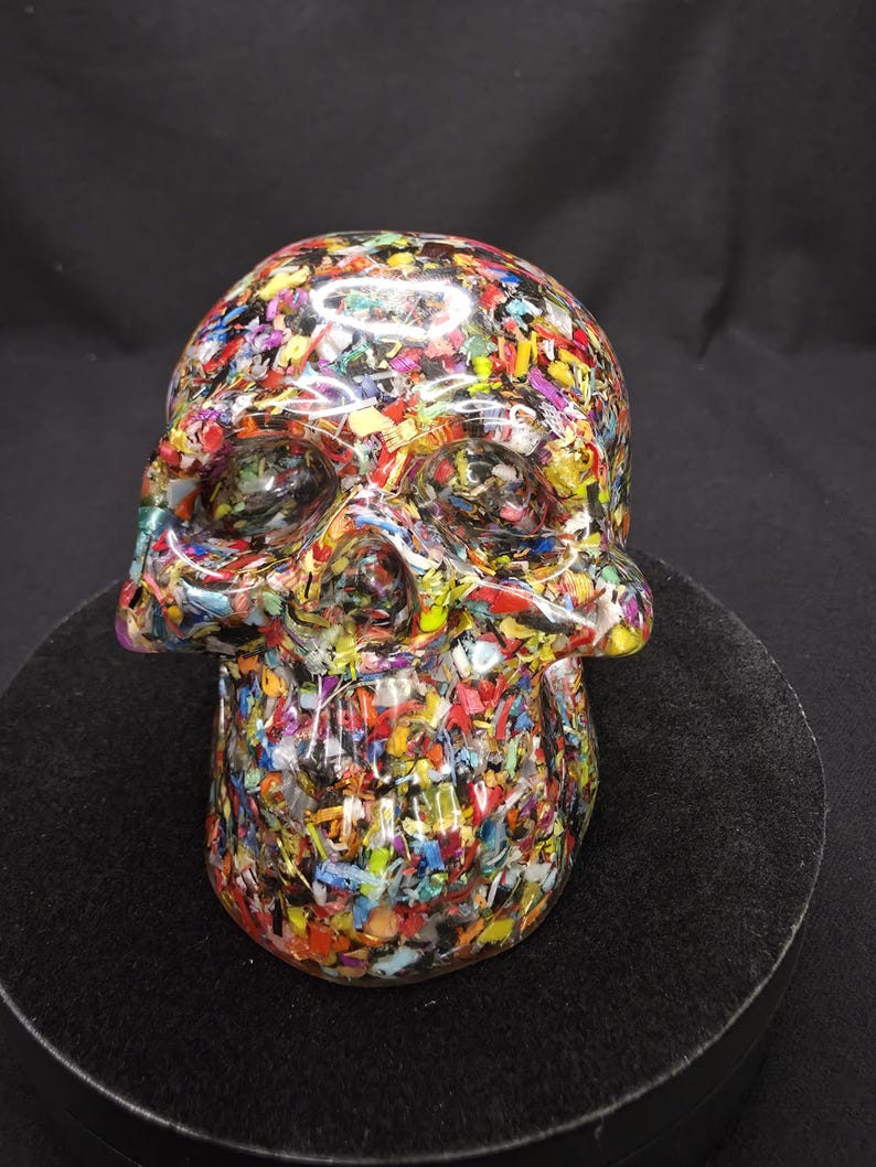 May include: A human skull sculpture crafted from clear resin embedded with a dense mixture of multicolored plastic confetti, including red, yellow, blue, green, and purple fragments, creating a vibrant, textured, and translucent appearance.