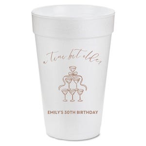 May include: White foam cup with a pink design that says "a tiny bit older" and has a drawing of a champagne glass tower. The text "Emily's 30th Birthday" is printed below the design.