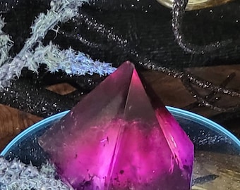 May include: A deep purple pyramid-shaped resin paperweight with a swirling, cloudy effect. The paperweight is sitting on a blue and white surface.