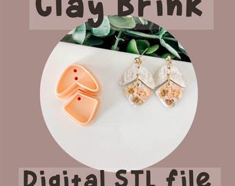 May include: A digital STL file for 3D printing a pair of earrings. The earrings are made of white clay with a textured surface and feature a floral design with pink and gold accents. The image also shows a mold for the earrings, which is made of pink plastic.