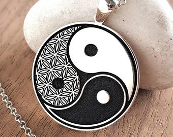 May include: A silver-toned circular pendant necklace featuring a black and white yin-yang symbol. One half of the yin-yang contains a detailed geometric flower of life pattern. The pendant hangs from a delicate silver-colored metal chain.