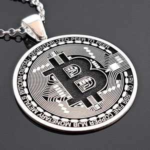 Op de afbeelding: Een zilveren ketting met een zwarte en zilveren hanger met een Bitcoin-symbool en de tekst "Bitcoin Digital Decentralized Peer to Peer."