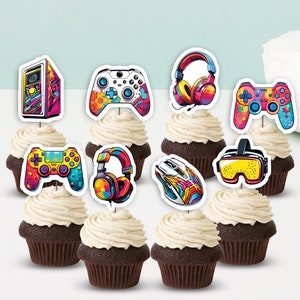 Może przedstawiać: Babeczki czekoladowe z białym lukrem, każda ozdobiona topperem o tematyce gier. Toppery przedstawiają kontrolery do gier, słuchawki, komputer, mysz i gogle VR, wszystkie w żywych kolorach.