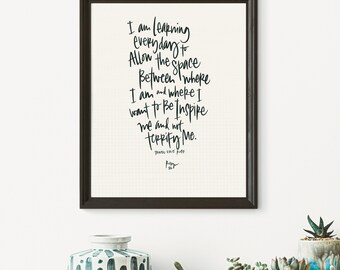 May include: A framed black and white print with a handwritten quote that reads "I am learning everyday to allow the space between where I am and where I want to be inspire me and not terrify me." The quote is attributed to "Trace Ellis Ross".