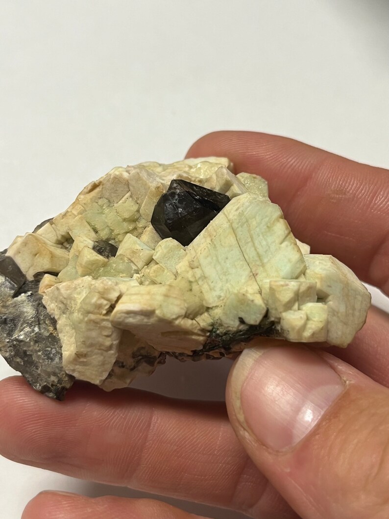 May include: A cluster of light green and white crystals with a dark brown crystal in the centre.