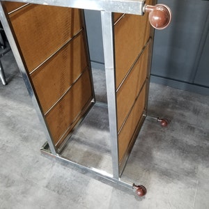 May include: A chrome metal rolling cart with four brown wheels. The cart has two shelves with wood-like panels.