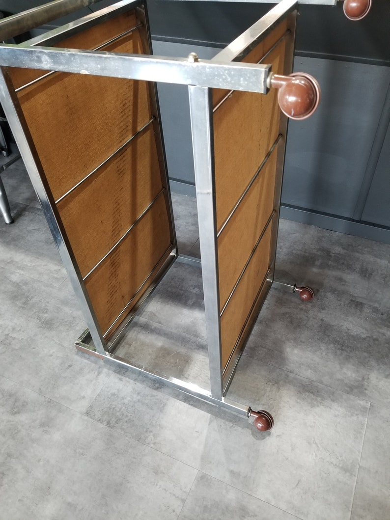 May include: A chrome metal rolling cart with four brown wheels. The cart has two shelves with wood-like panels.