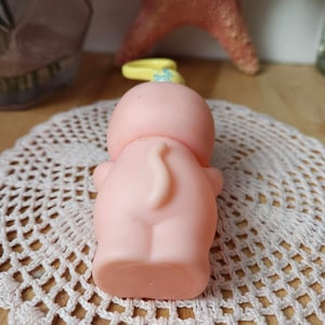 Puede incluir: Un juguete de goma rosa con una cola amarilla y una cabeza azul y amarilla. El juguete est&aacute; sentado en un encaje blanco de ganchillo.