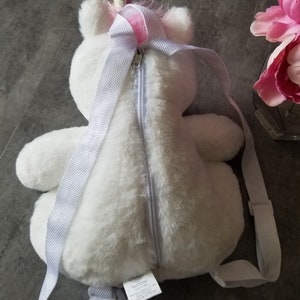May include: White plush unicorn backpack with a pink and gold horn. The backpack has a zipper closure and white straps.
