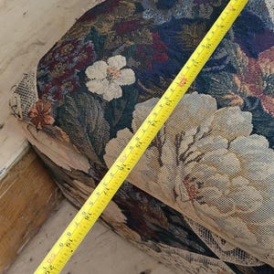 May include: A close-up of a floral patterned fabric with a yellow measuring tape on top. The tape measures 21 inches.