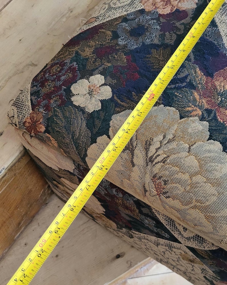 May include: A close-up of a floral patterned fabric with a yellow measuring tape on top. The tape measures 21 inches.