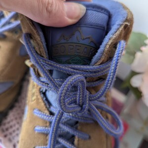 May include: Tan leather hiking boots with blue laces and a blue lining. The boots have a logo on the tongue that says "SO PEAK" with the words "Hi-Tec" underneath.