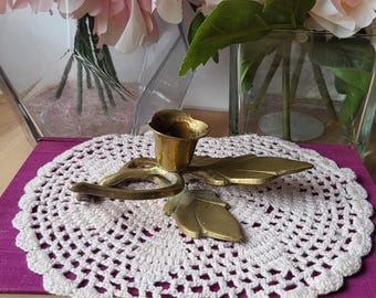 Puede incluir: Un candelero de latón con un diseño de hojas. El candelero está sobre un encaje de ganchillo blanco sobre un libro morado.