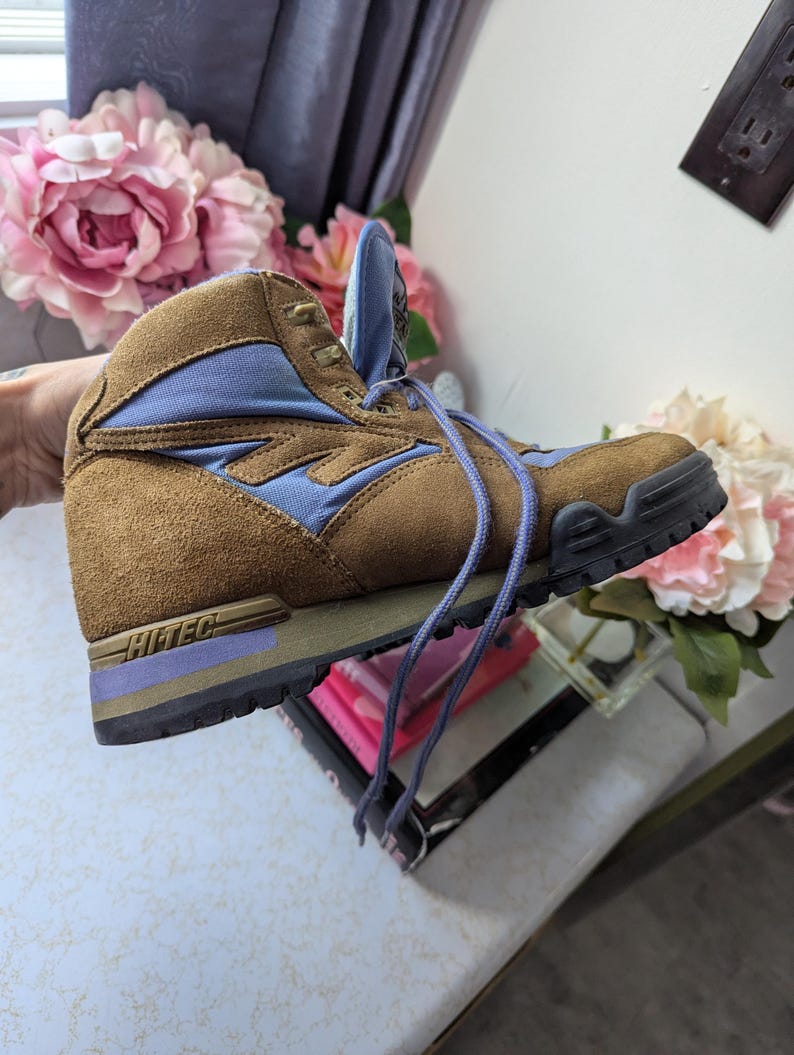 May include: Brown suede hiking boots with blue accents and a purple Hi-Tec logo on the side. The boots have a lace-up closure and a rugged outsole.