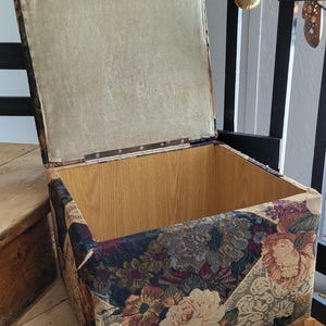 May include: A floral patterned storage ottoman with a hinged lid. The lid is open, revealing a wooden interior. The ottoman is sitting on wooden steps.