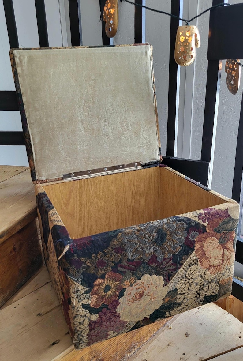 May include: A floral patterned storage ottoman with a hinged lid. The lid is open, revealing a wooden interior. The ottoman is sitting on wooden steps.