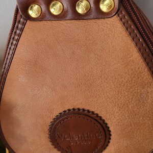 May include: A brown leather satchel bag with gold accents and a circular logo that reads "Valentino di Paolo".