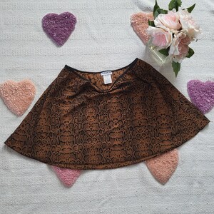 May include: A brown and black snakeskin print skirt with a flared silhouette. The skirt is set against a white background with heart-shaped decorations in shades of pink and purple. A small bouquet of pink flowers sits in a glass vase.