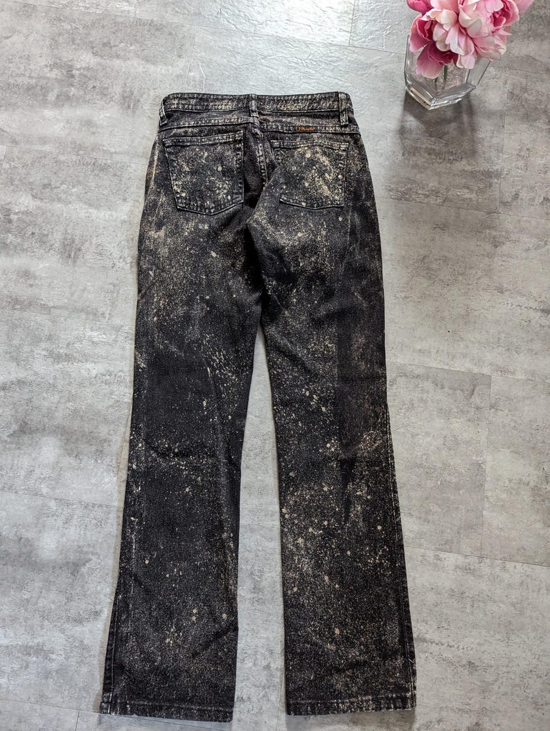 May include: Black denim jeans with a bleach splatter pattern. The jeans have a bootcut leg style.