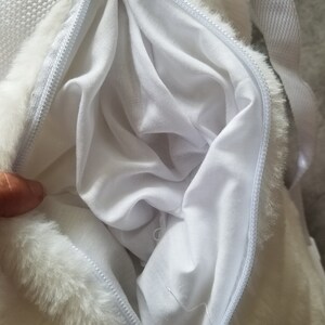 May include: White faux fur backpack with a zipper opening. The inside of the backpack is lined with white fabric.