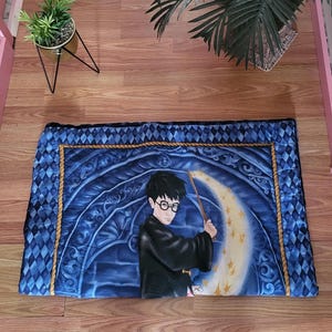 Peut inclure: Une couverture en coton matelassée bleue avec un motif Harry Potter. La couverture représente une lune croissante, des étoiles et Harry Potter lançant un sort avec sa baguette.