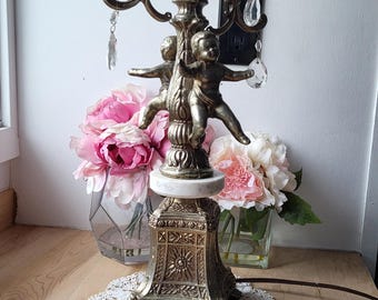 Könnte beinhalten: Eine goldfarbene Tischlampe mit einem weißen Marmorsockel und Cherub-Akzenten. Die Lampe hat Kristall-Akzente und ein zartes Blumenmuster.