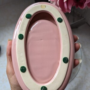 May include: Pink oval ceramic dish with a white rim and green felt dots on the bottom.