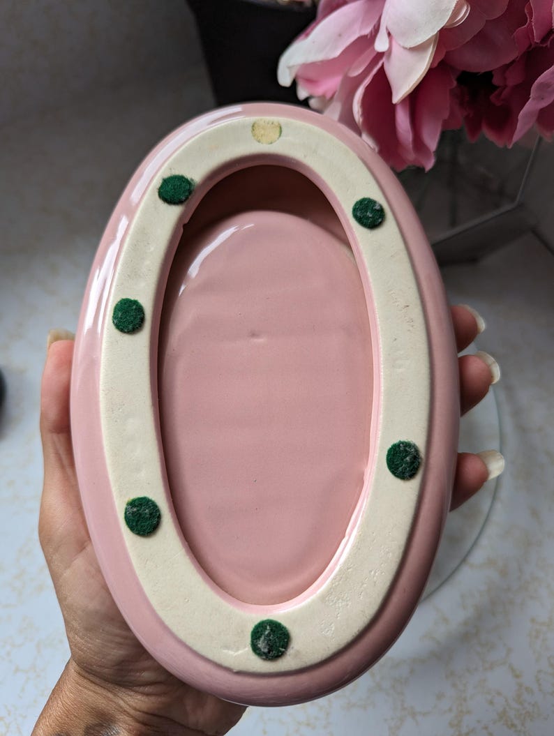 May include: Pink oval ceramic dish with a white rim and green felt dots on the bottom.