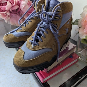 May include: Brown and blue suede hiking boots with a lace-up closure. The boots have a black rubber sole and are sitting on top of a stack of books.