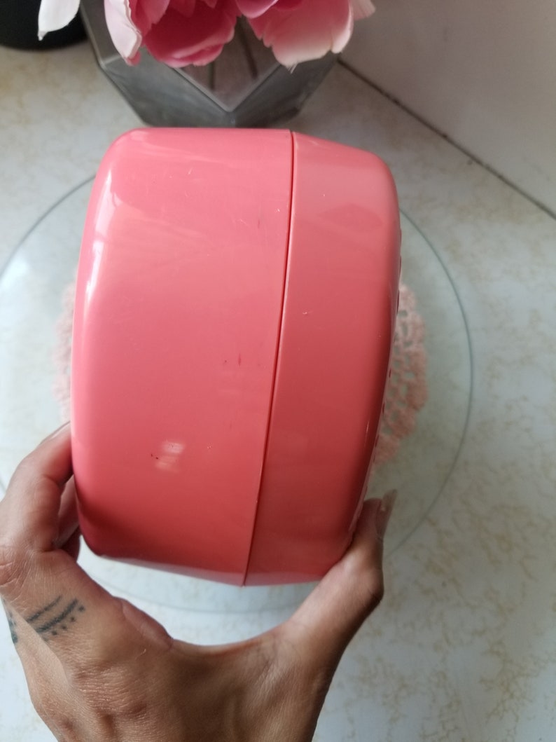 May include: A pink plastic container with a rounded shape and a smooth surface. The container is closed and has a slight seam running around the middle.