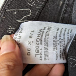 May include: A white tag with black text attached to a pair of black jeans. The tag lists the size as 1/2 x 36, the style as WRQ20BL, and the number 9L000028P 71647. The tag also states that the jeans are made in Mexico with fabric from the U.S. and are 99% cotton and 1% spandex.