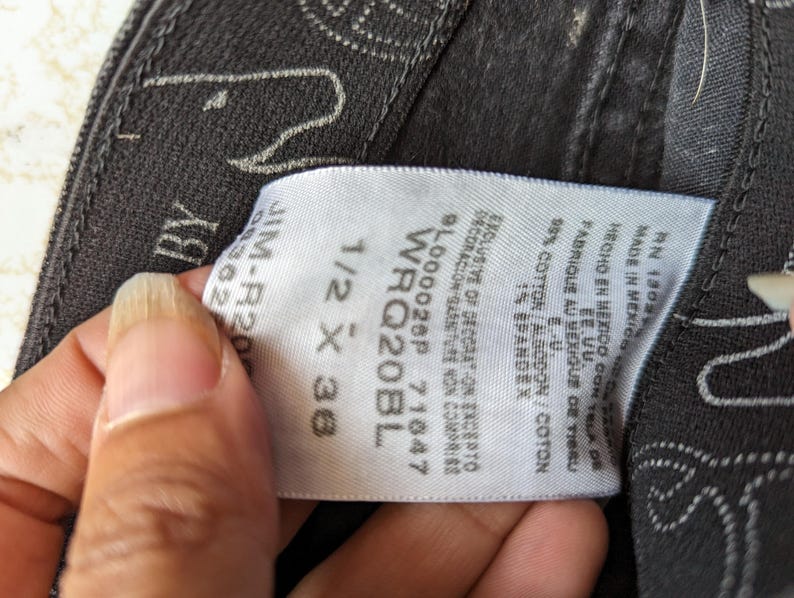 May include: A white tag with black text attached to a pair of black jeans. The tag lists the size as 1/2 x 36, the style as WRQ20BL, and the number 9L000028P 71647. The tag also states that the jeans are made in Mexico with fabric from the U.S. and are 99% cotton and 1% spandex.