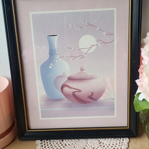 Op de afbeelding: Een ingelijste print van een stilleven met twee vazen, een blauwe en een roze, met een tak met witte bloesems en een volle maan op de achtergrond.