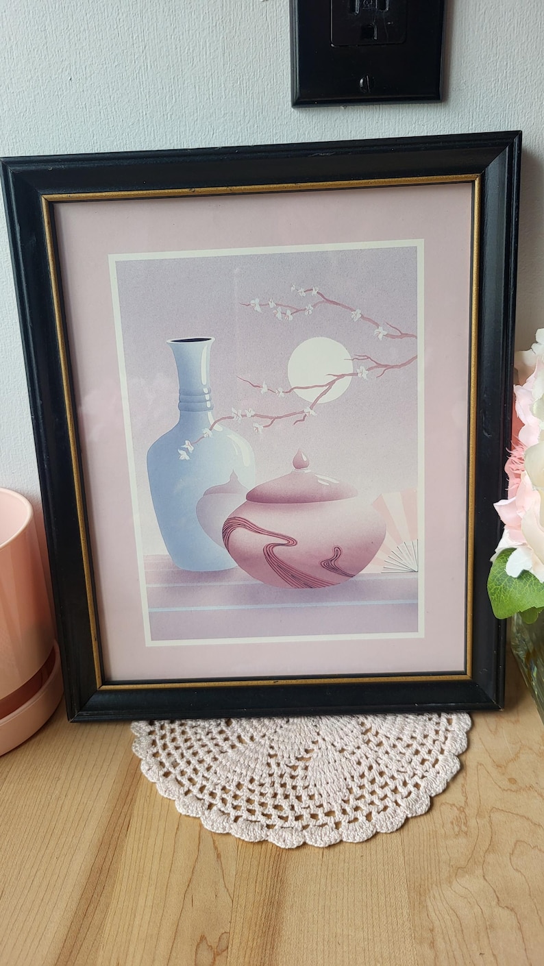 Op de afbeelding: Een ingelijste print van een stilleven met twee vazen, een blauwe en een roze, met een tak met witte bloesems en een volle maan op de achtergrond.