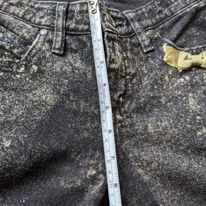 May include: Black acid wash denim jeans with a yellow bow detail. The jeans have a measurement tape running vertically along the side, measuring 9 inches.