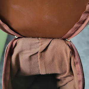 May include: A brown leather bag with a zipper closure. The bag is open and the inside is lined with a brown fabric.