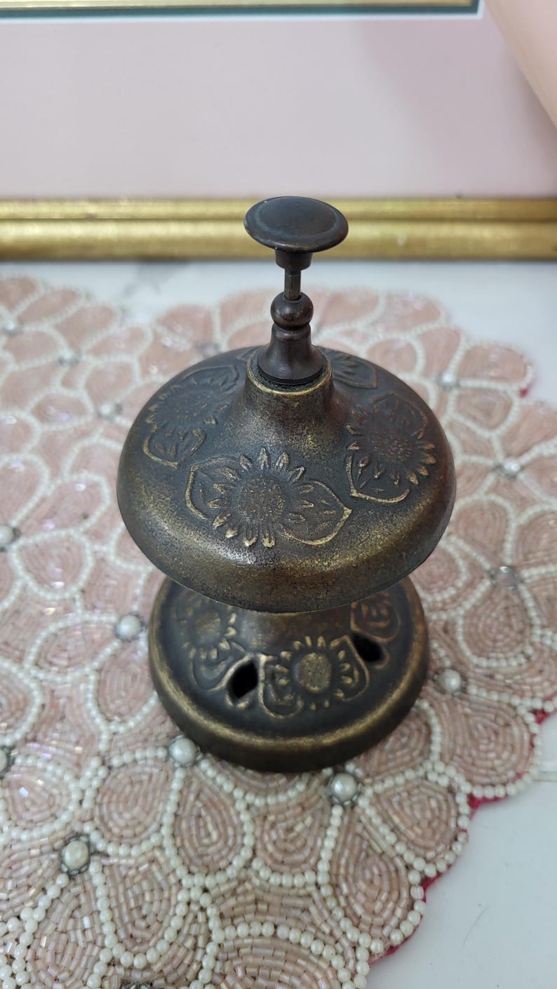Puede incluir: Un quemador de incienso antiguo de color bronce con motivos florales. El quemador tiene una base redonda y una parte superior abovedada con un peque&ntilde;o asa. El dise&ntilde;o incluye patrones recortados alrededor de la base y grabados florales en la parte superior.