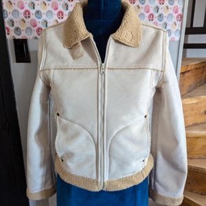 May include: A cream-coloured suede jacket with a brown faux fur collar and lining. The jacket has a zip closure and two pockets.