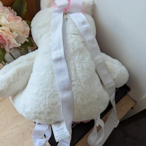 May include: White plush unicorn backpack with pink accents and a zipper closure. The backpack has adjustable straps.