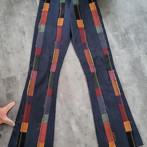 Può includere: Pantaloni a zampa d'elefante in denim blu con dettagli di patchwork colorati sui lati. Il patchwork è realizzato con tessuti e colori diversi, tra cui rosso, arancione, giallo, verde e blu.