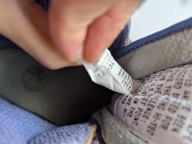 May include: Close-up of the inside of a blue shoe with a white tag that reads "TECT" and "THE CHALLENGE: BELIEVE IN THE TIME. HI-TECH SST POINT", and a black and white logo.