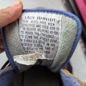 May include: A close-up of a blue and white label with the text "Lady Rainier" and a description of the boots' features. The text reads: "These boots have been developed and used for the record breaking hi-tec 50 peaks. The challenge: to climb the highest point in every U.S. state in the shortest overall time. Hi-tech flat earth."