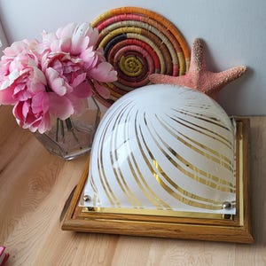 Pode incluir: Uma luminária de teto branca com acabamento dourado e um abajur de vidro branco com listras douradas. O abajur tem a forma de uma cúpula e assenta sobre uma base quadrada.