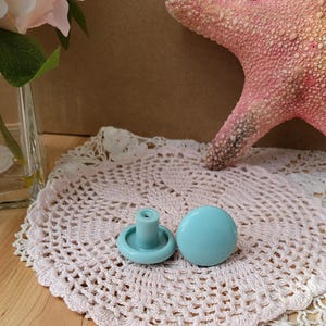Peut inclure: Deux boutons de cabinet de couleur bleu clair de forme ronde. Les boutons sont sur un napperon en crochet blanc.
