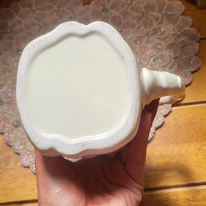 May include: Cream-colored ceramic mug with a handle. The mug has a rounded base and a smooth, glossy finish. The handle is small and curved. The mug is likely for beverages and is suitable for home or office use.
