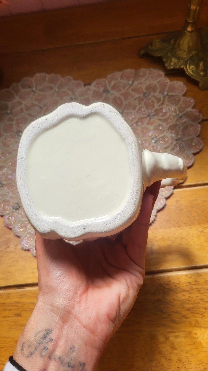 May include: Cream-colored ceramic mug with a handle. The mug has a rounded base and a smooth, glossy finish. The handle is small and curved. The mug is likely for beverages and is suitable for home or office use.