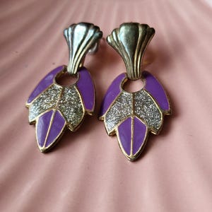 May include: A pair of dangle earrings with a silver and gold finish. The earrings feature a purple and silver leaf design with glitter accents.